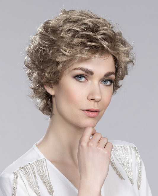 "Perruque femme City, idéale pour pelade et alopécie. Boucles souples et volumineuses encadrant le visage avec élégance. Frange légère pour mettre en valeur le regard et créer un style urbain chic.