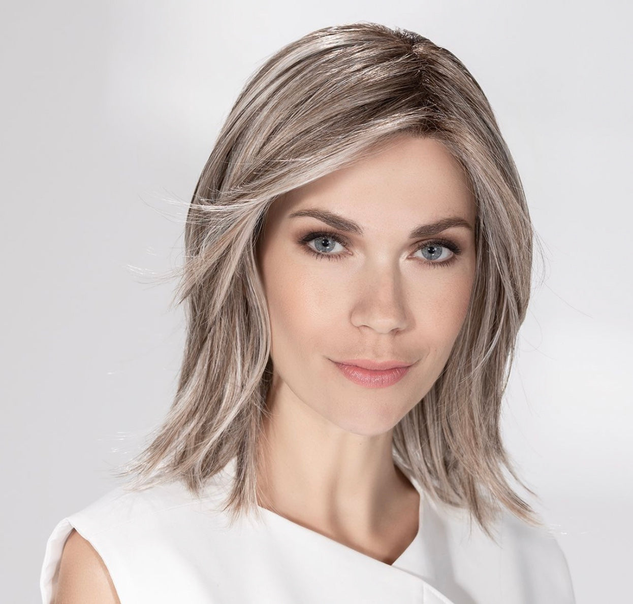 Perruque Whisper Comfort de la collection Hair Society Ellen Wille, coupe mi-longue effleurant les épaules, chevelure lisse et soignée avec mèche délicate, confort médical exceptionnel et discrétion optimale, fibre synthétique résistante à la chaleur permettant lissage, boucles ou brushing jusqu’à 130°C.
